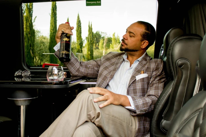 A well dressed man examining a bottle of wine while sitting in a luxuriant customized sprinter during a bespoke wine tour
